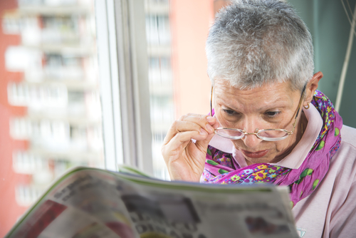 An elderly woman looking over her glasses to read