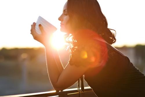 woman holding cup of coffee with sunrise in the background 